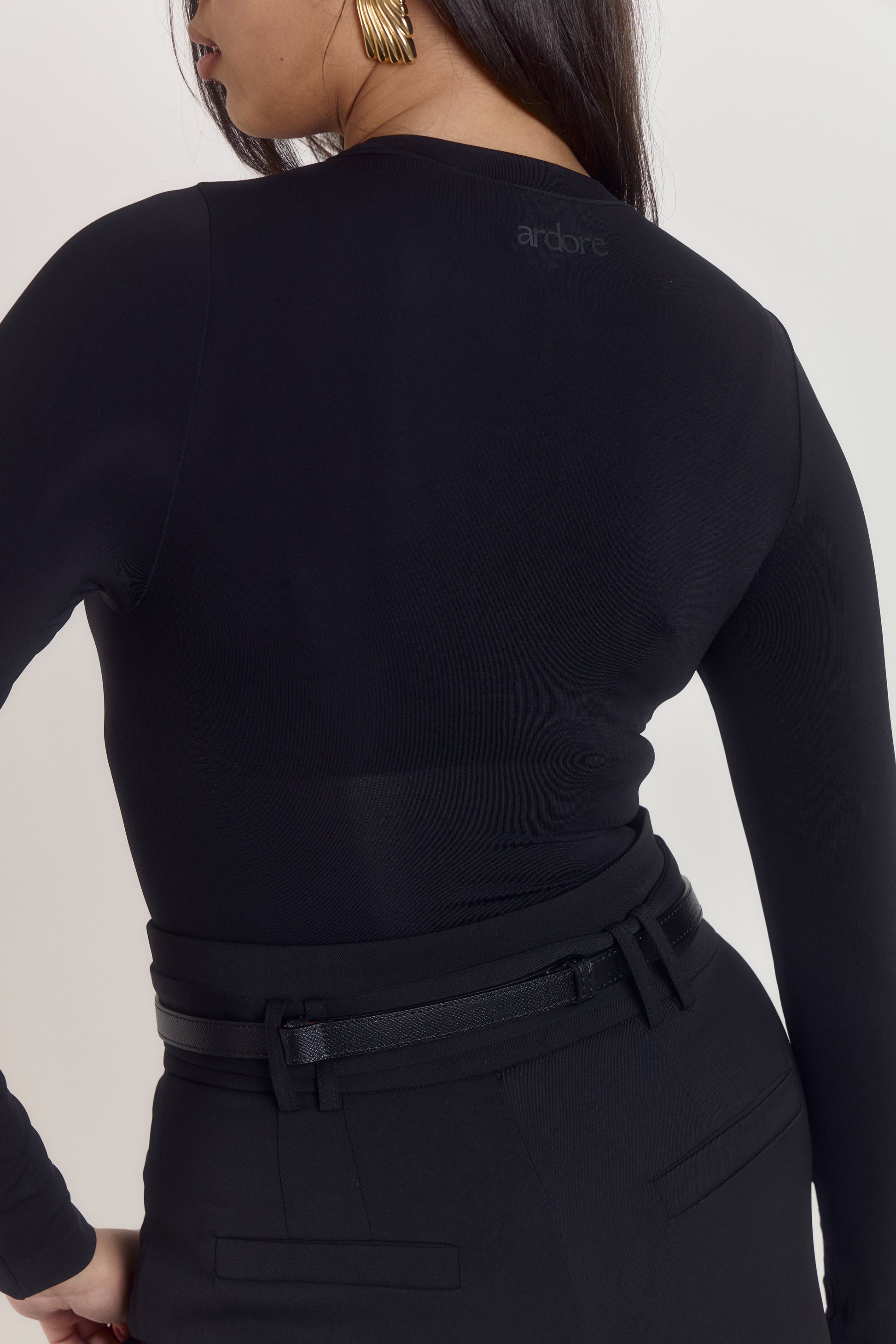 Model wearing black long sleeve shapewear bodysuit with waist compression zone and sculpting contour fit.