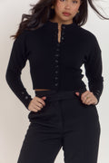Close detail of sculpted waistline on structured black cardigan with high rounded neckline.
