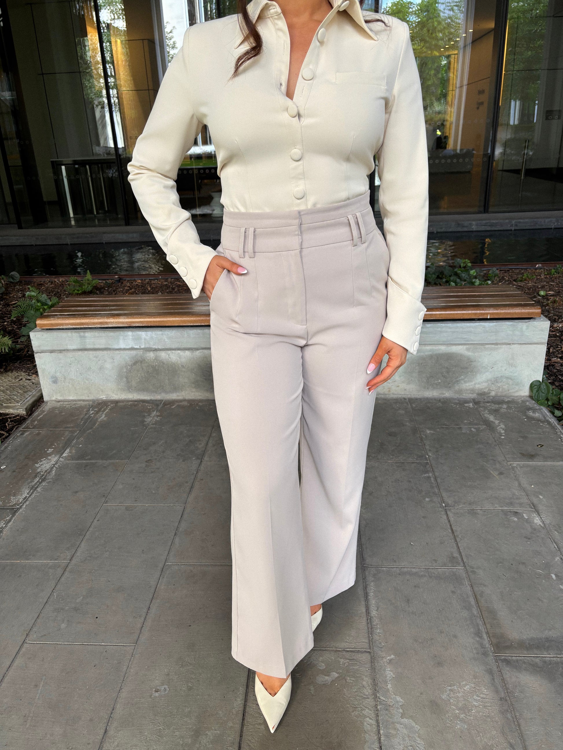 Front view of tailoring wide leg trousers in chai latté paired with a crème blouse by Ardore London, showcasing a refined and contemporary silhouette.