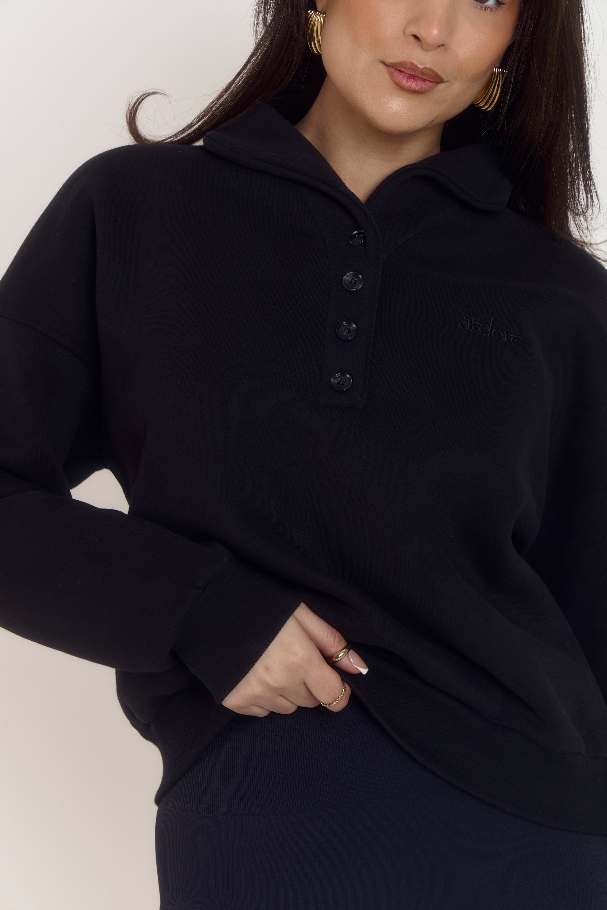 Women’s oversized black cotton sweater with structured collar, quarter button front and ultra-soft interior lining.