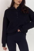 Model wearing oversized heavyweight cotton collared quarter button sweater in classic noir black with tortoiseshell buttons and structured funnel neckline.