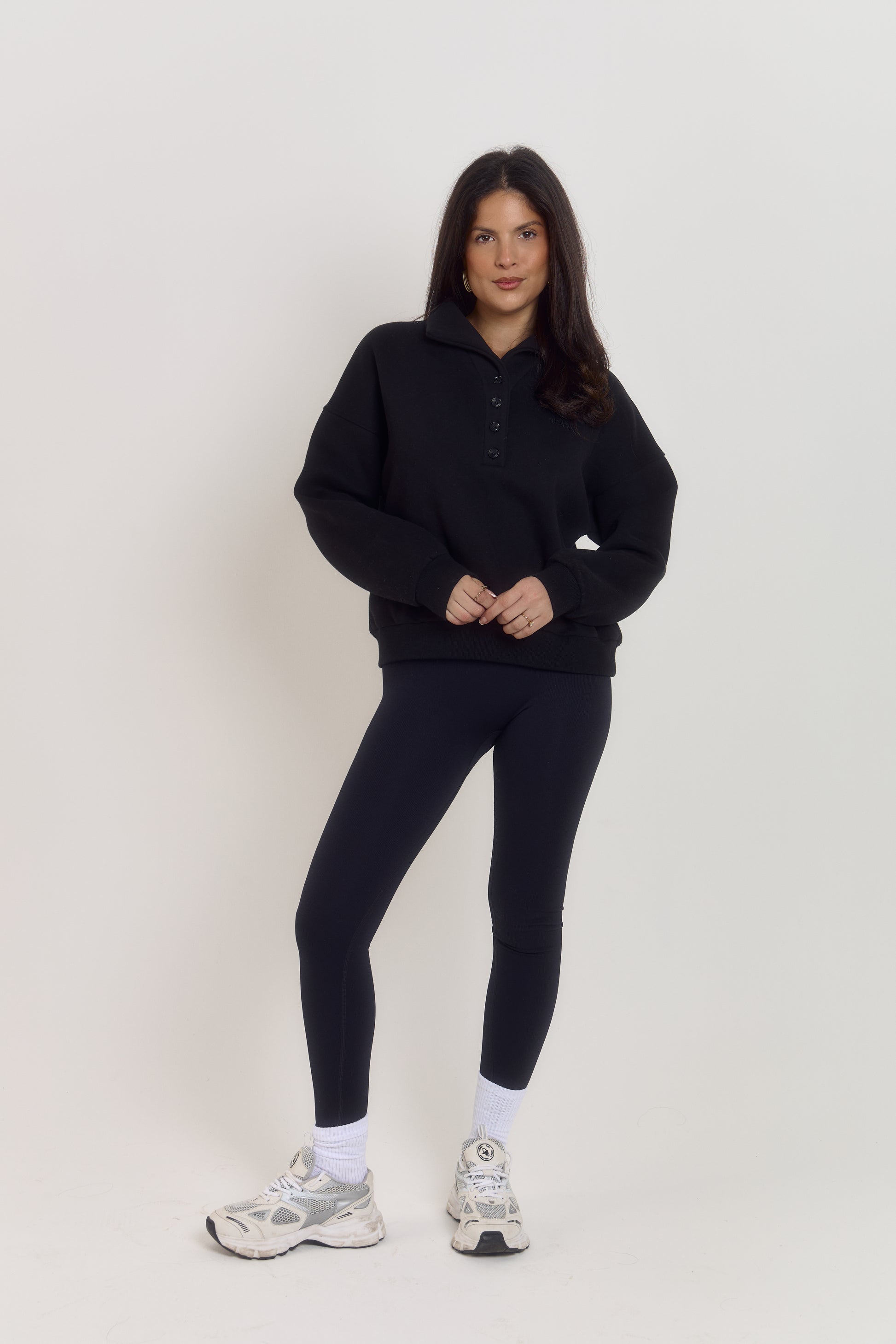 Model wearing Ardore structured oversized quarter button sweater in classic noir black, heavyweight fabric with tortoiseshell buttons and funnel neck collar styled up.