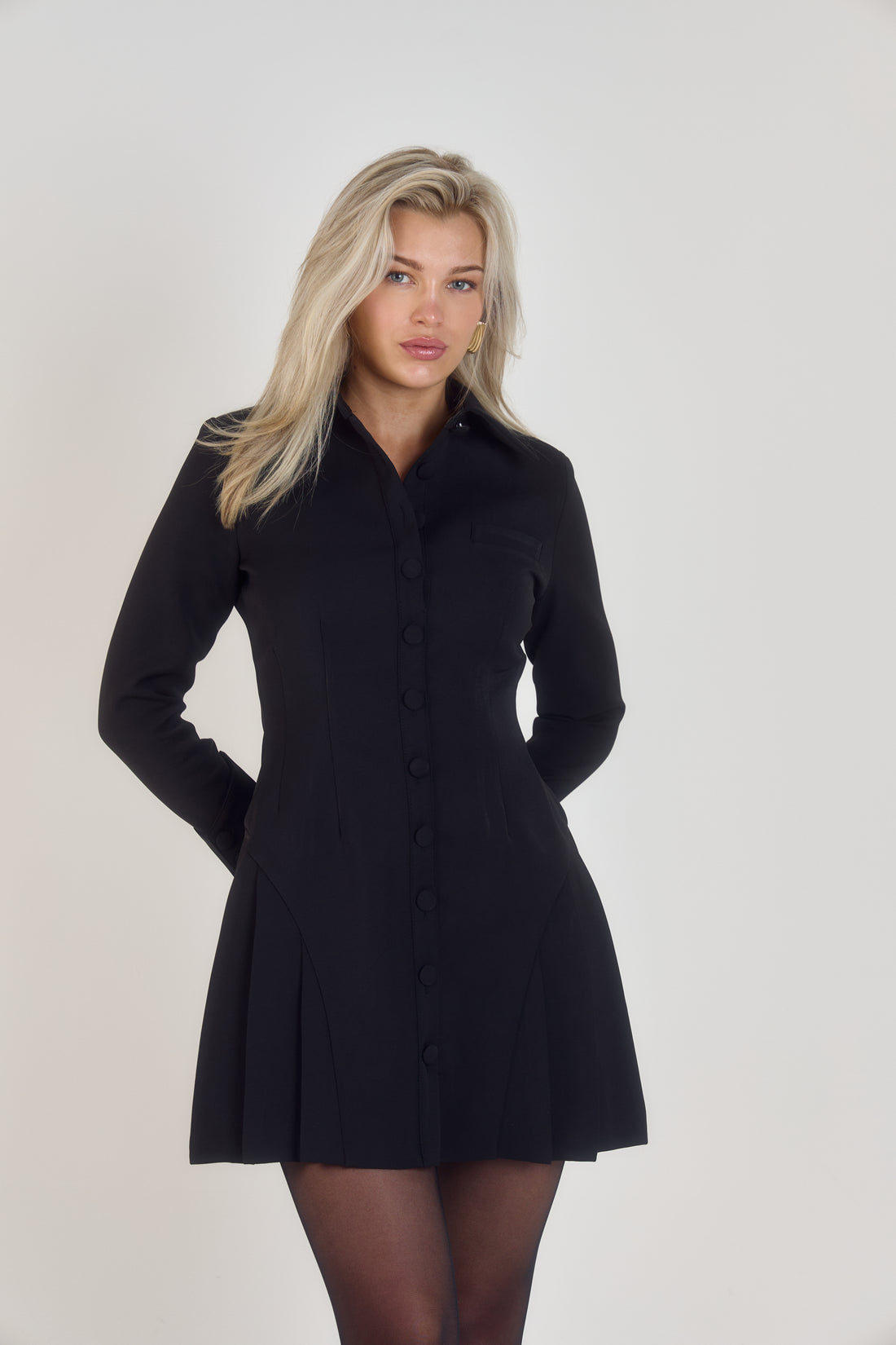 Elegant black structured long sleeve pleated mini dress with flattering curvy hip shape, timeless old money aesthetic, exaggerated 1970s-inspired collar, sculpted silhouette, and unique small designer details.