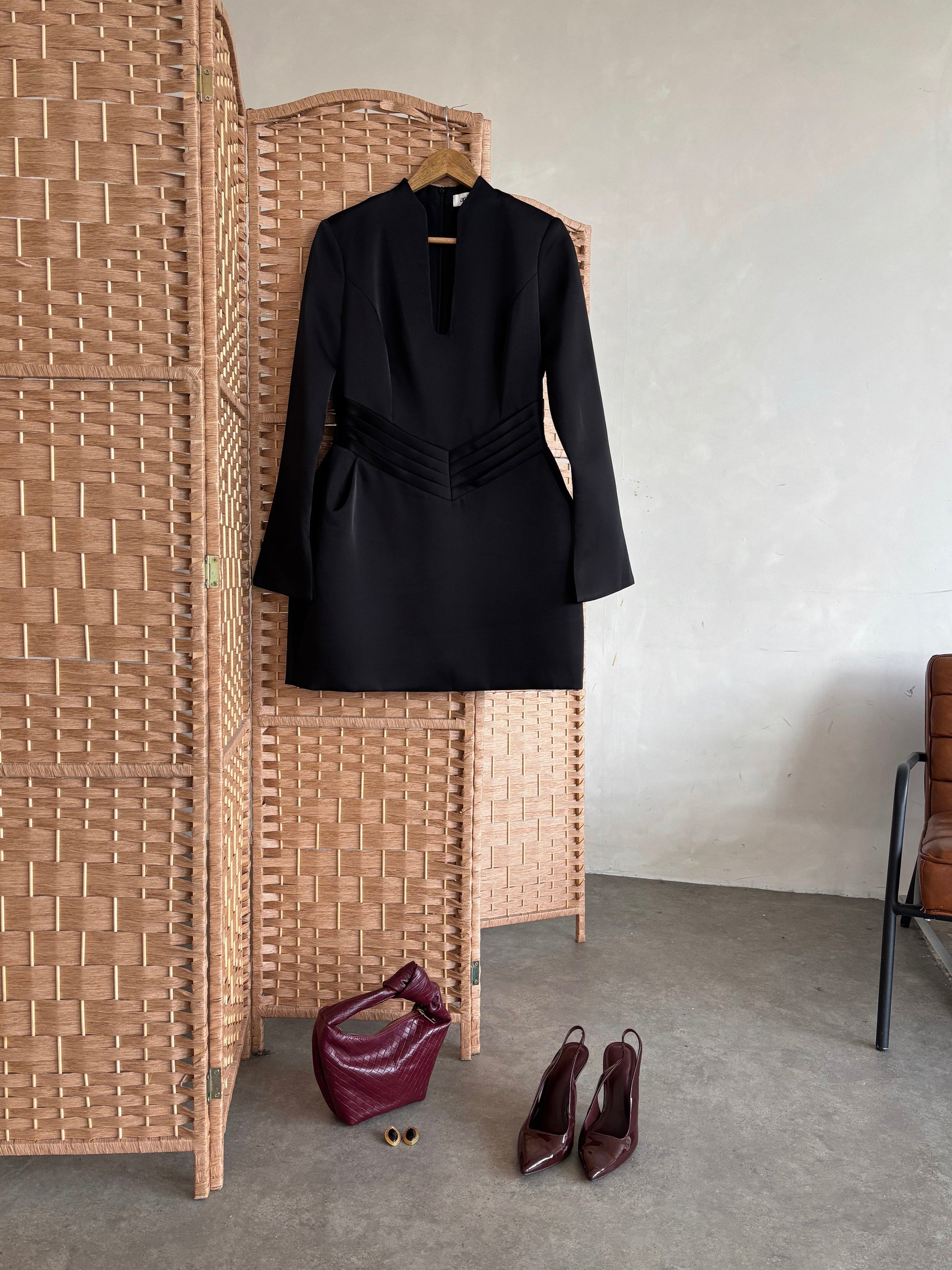 Black dress on a hanger next to woven screen and shoes on the floor