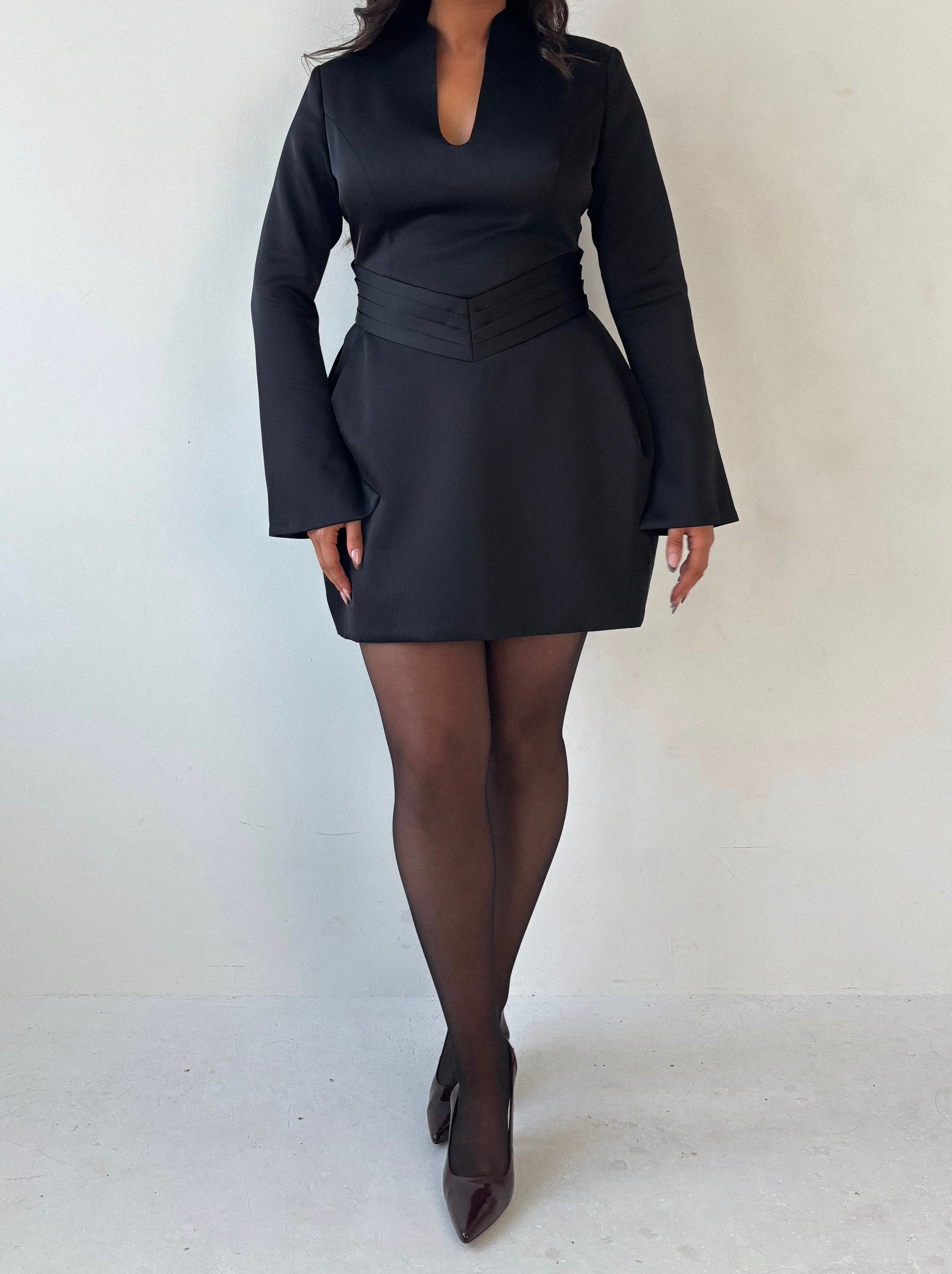 Close-up of Ardore London black satin split sleeve mini dress, featuring a pleated V-shaped waist for a flattering fit, an elegant A-line skirt, and fluid split sleeves—crafted in lustrous satin for a sleek winter-ready silhouette with graceful movement and modern edge.