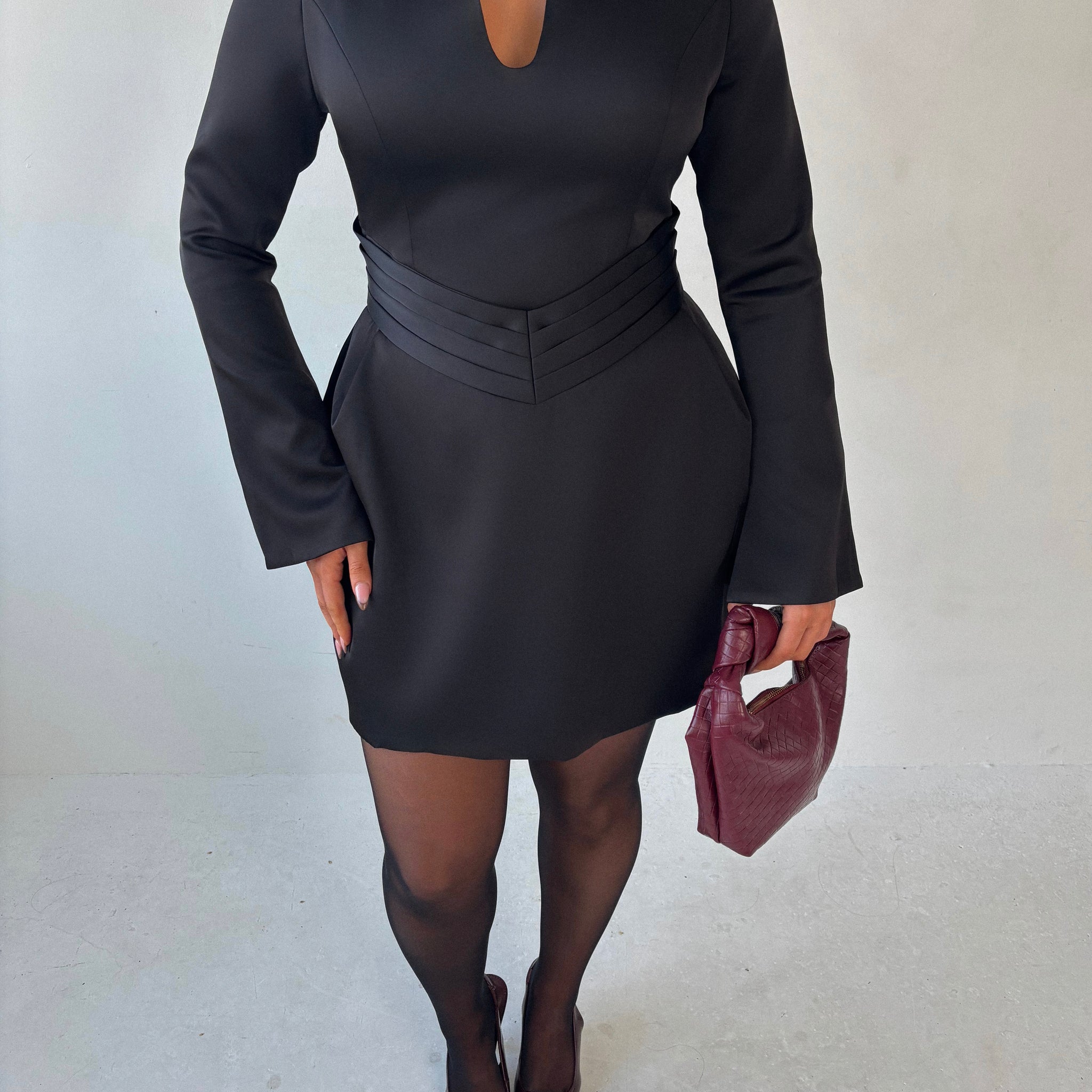 Close-up of Ardore London black satin split sleeve mini dress, featuring a pleated V-shaped waist for a flattering fit, an elegant A-line skirt, and fluid split sleeves—crafted in lustrous satin for a sleek winter-ready silhouette with graceful movement and modern edge.