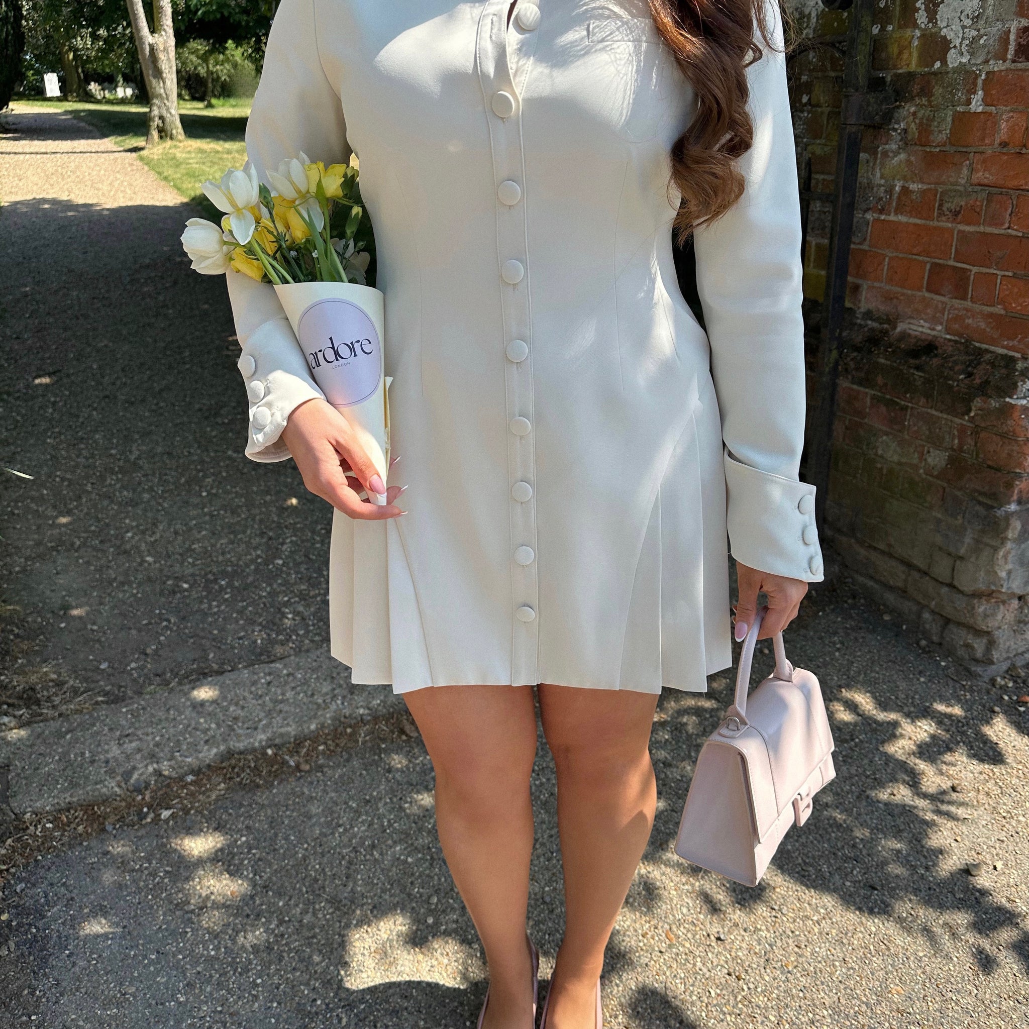 Close-up of Ardore London Vanilla Crème structured long sleeve pleated mini dress showcasing precise tailoring, pleated skirt, textured fabric, and defined sleeve construction.