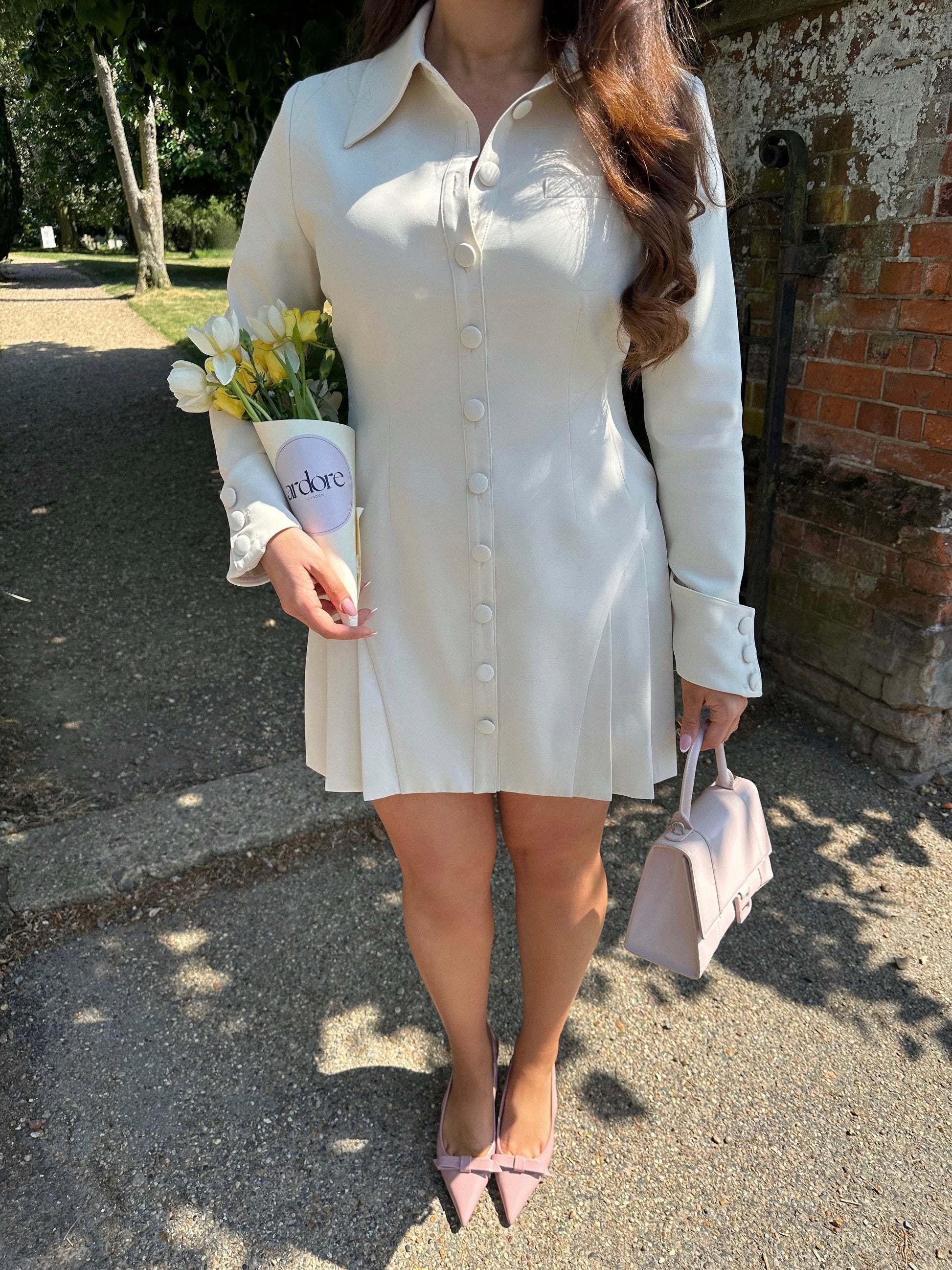 Close-up of Ardore London Vanilla Crème structured long sleeve pleated mini dress showcasing precise tailoring, pleated skirt, textured fabric, and defined sleeve construction.