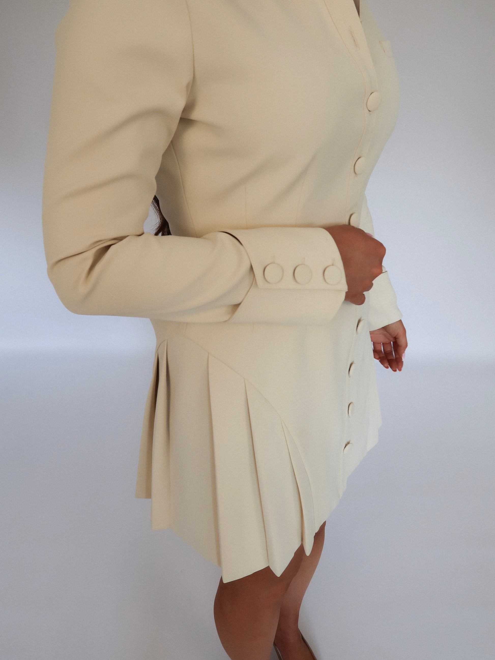 Side shot of Ardore London Vanilla Crème structured mini dress, emphasizing the precise tailoring, pleated skirt, and sculpted sleeve design.